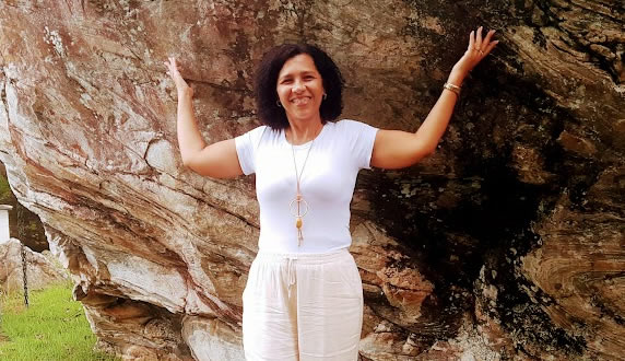 Mulher em pé ao lado de uma rocha  Descrição gerada automaticamente com confiança média